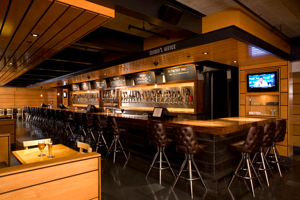 The back bar is a trophy wall that showcases each unique tap in its glory, and interior walls are then finished in wood panels in a luscious honey color with linear patterns to help create the effect of an elongated space.