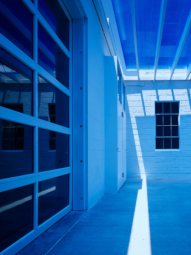 Detail under the entry canopy showing the blue polycarbonate and the existing steel windows. The sun creates magical changes throughout the day. The space remains a deep blue during daylight hours.