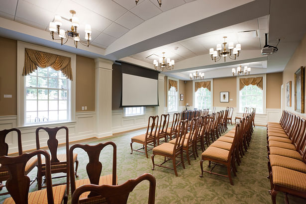 Wood paneling and trim in the wings of the building are painted to distinguish these spaces from the central block. In this large meeting room historic light fixtures were restored and reused.