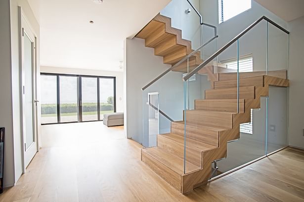 Floating Staircase with White Oak Wood & StarFire Glass Railings keep the beach feel throughout this waterfront property.