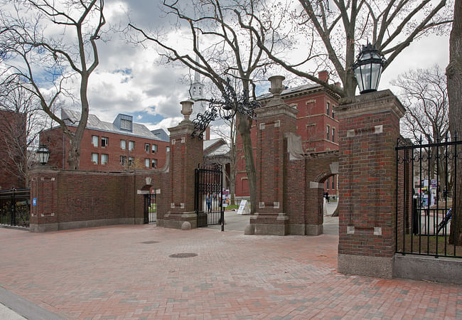 The U-shaped entry consists of a central carriage gate flanked by urn-topped brick piers and arched foot gates. The thin spire of Harvard’s Memorial Church rises in the background. Image credit: Ralph Lieberman
