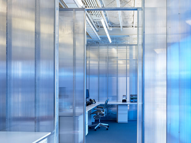 A typical open office space created by clear polycarbonate panels. The perimeter blue panels provide a softened blue hue. 
