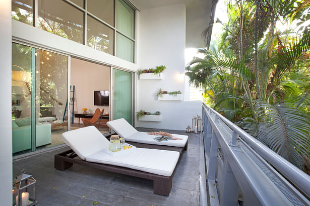 Looking out onto a side garden densely planted with tropical floiage, the wide deck has been finished with a porcelain tile with a wood-grain surface. the double sun chaise with built-in center table was sourced from Addison House. 